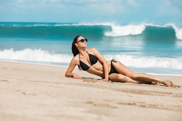 Yakın çekim güzel lüks ince ve tabaklanmış kız sahilde okyanus siyah bir bikini. Seksi tabaklanmış vücut, düz bir karın, mükemmel rakam. Tropik bir adada dinlenmek.