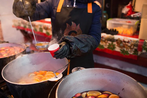 Hot gluhwein or mulled wine in a cauldron at fair, local treat, warm and spicy. A hot wholesome traditional citrus drink on fair. Vitamins in the winter festival. Pour the drink into a glass or a cup.
