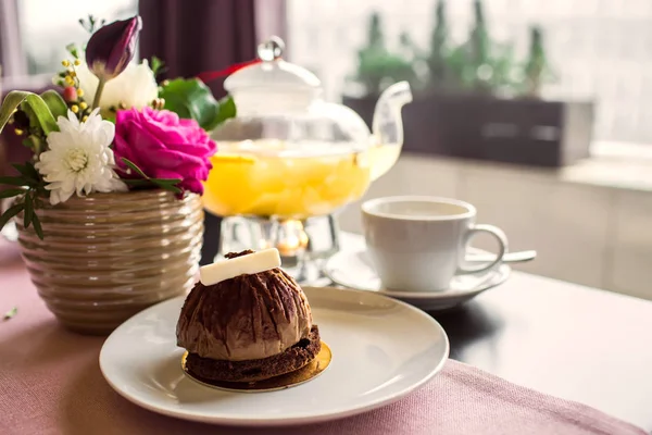 Chocolate truffle cake dessert with white chocolate. Pineapple tea with a transparent glass teapot. Citrus vitamin tea and a beautiful bouquet of flowers with roses, daisies and tulips on the table.