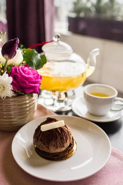 Çikolata pasta tatlı beyaz çikolata ile. Şeffaf cam demlik çay ananas. Narenciye vitamini çay ve güzel bir buket çiçek gül, papatya ve Lale masada. — Stok fotoğraf