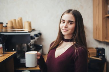 Beyaz bardakta kahve içeceği hazırlıyorum. Güzel barista kızı elinde beyaz bir fincan kahve tutuyor..