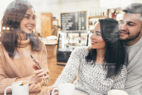 A group of friends who drink coffee or tea together. Two women and men in a cafe, talk, laugh and enjoy their time. Friendship with real people models.