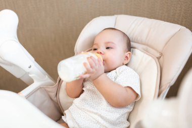 Bebek sandalyede yemek yiyor. Annem bebeği püre yiyecekle besler. Bebeğin ilk beslenmesi. Çocuk kendi başına şişeden yiyip içiyor..