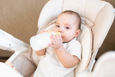 Bebek sandalyede yemek yiyor. Annem bebeği püre yiyecekle besler. Bebeğin ilk beslenmesi. Çocuk kendi başına şişeden yiyip içiyor..