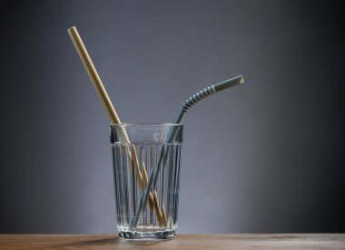 A refillable glass cup with a  straw from reeds and a plastic straw 