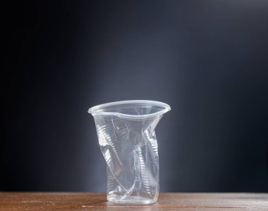 Used disposable plastic cup on a wooden table on a gray background.