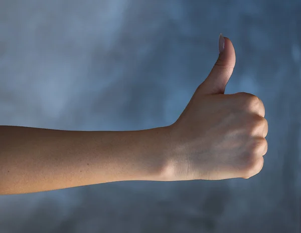 Female hand shows a sign that symbolizes like on a gray background. — Stockfoto