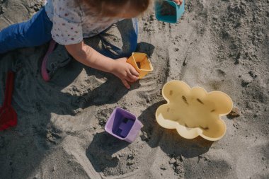 Küçük kız kumların üzerinde kutular ve kum küreğiyle oynuyor.