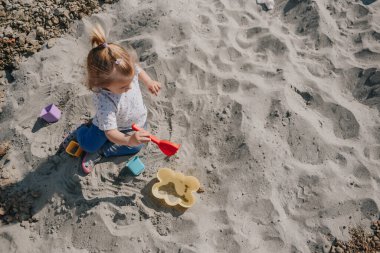 Küçük kız kumların üzerinde kutular ve kum küreğiyle oynuyor.