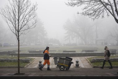 BELGRAD, SERBIA - 16 HAZİRAN 2020: Sırp başkenti üzerindeki gökyüzüne ağır sis hakim olduğu için sokakta yürüyen servis elemanı ve yaya temizliği. Birkaç gündür şehirde yoğun bir kirlilik bulutu görülüyor.