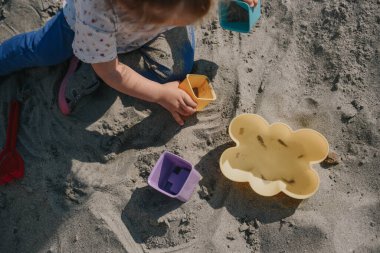 Küçük kız kumların üzerinde kutular ve kum küreğiyle oynuyor.