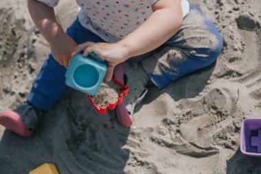 Küçük kız kumların üzerinde kutular ve kum küreğiyle oynuyor.