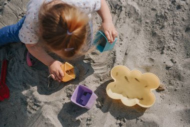 Küçük kız kumların üzerinde kutular ve kum küreğiyle oynuyor.