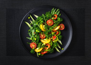 Yukarıdan siyah tabak manzaralı taze sebze salatası.