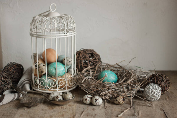 Painted and quail eggs in decorative cage and nest on old wooden table