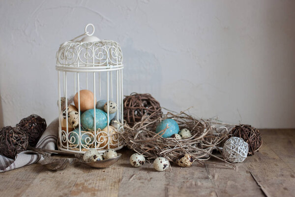 Painted and quail eggs in decorative cage and nest on old wooden table