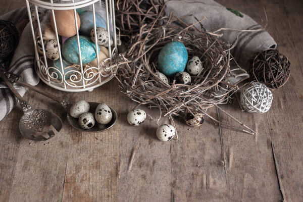 Painted and quail eggs in decorative cage and nest on old wooden table