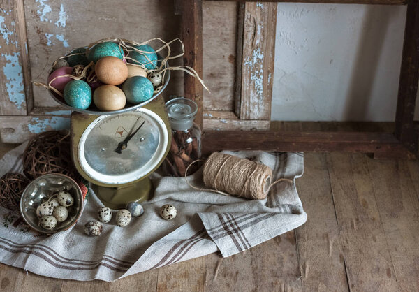 Rustic still life with old scale, Easter eggs, bottle with aroma spices and linen cloth on wooden table.
