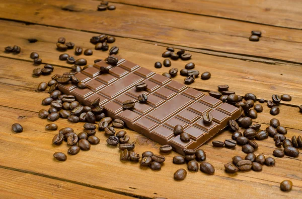 Grains of coffee and bar of chocolate on an old wooden table.