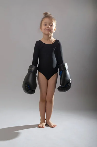 Niña con guantes de boxeo de papá sobre un fondo gris . — Foto de Stock