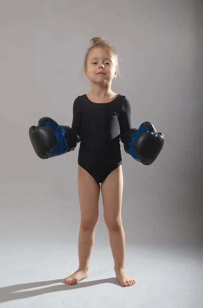 Niña con guantes de boxeo de papá sobre un fondo gris . — Foto de Stock