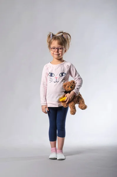 Hermosa chica con un oso de peluche sobre un fondo gris . — Foto de Stock