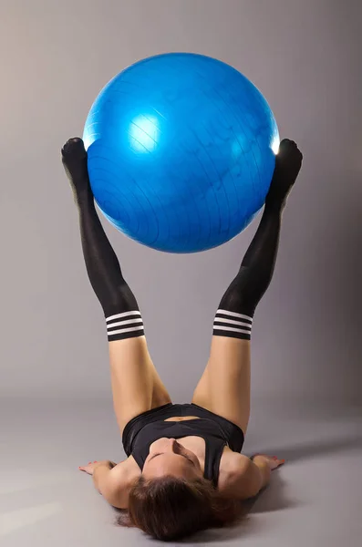 Mujer joven haciendo ejercicios con fitball, sobre un fondo gris . — Foto de Stock