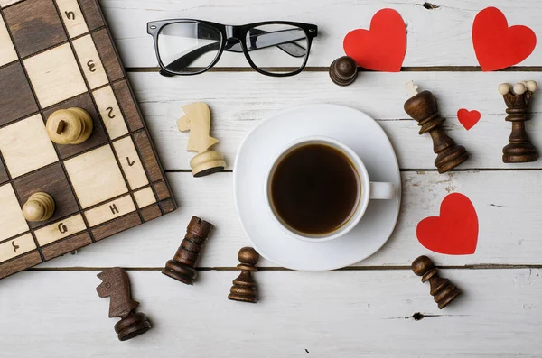 Чашка кави, окуляри та шахові фігури на дерев'яному столі, зверху — стокове фото