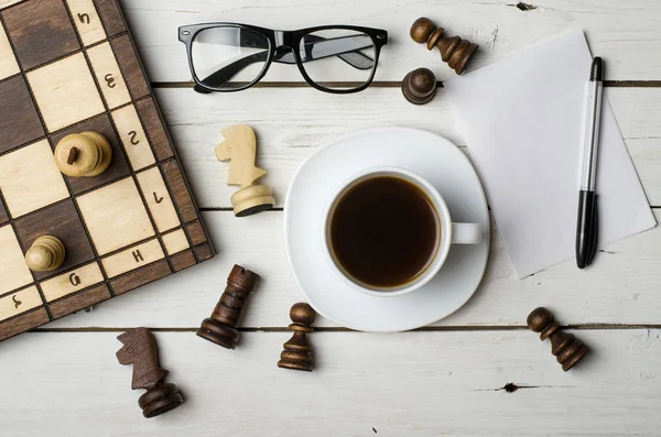 Чашка гарячої кави і шахові фігури на дерев'яному столі, вид зверху — стокове фото