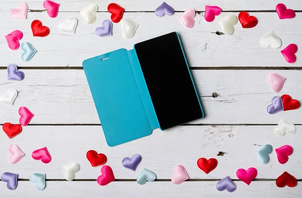 Hearts scattered on a wooden table and a smartphone. — Stock Photo, Image