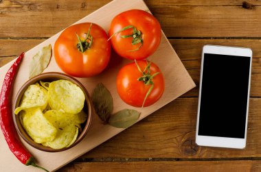 Ahşap bir masa, domates ve smartphon bir kapta patates cips