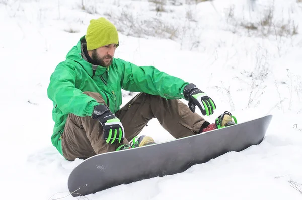 Чоловік сноубордист сидить на снігу . — стокове фото