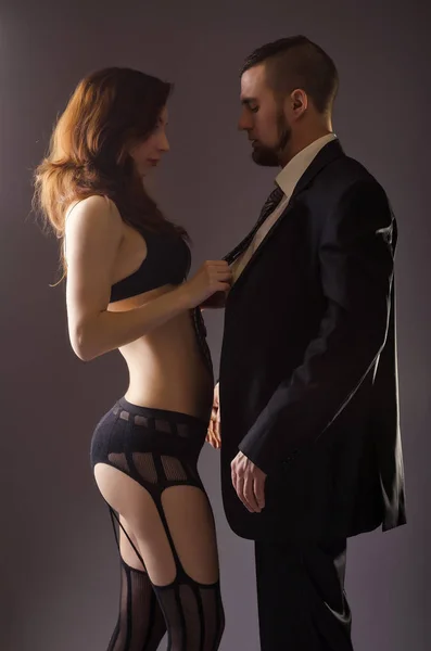 Un homme en costume noir et une femme en lingerie, sur un dos gris — Photo