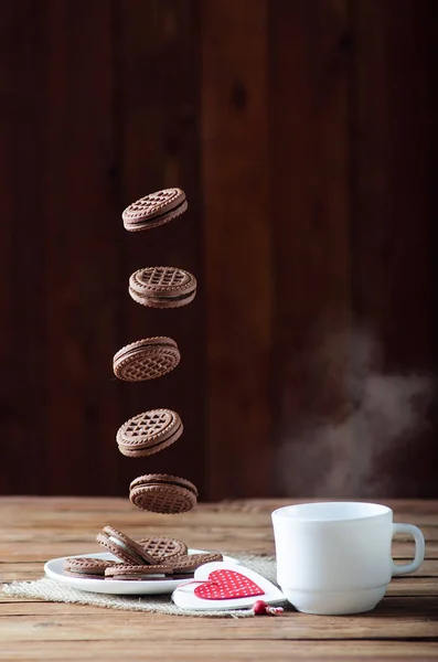 Pliki cookie w czasie lotu i filiżankę gorącej herbaty, zbliżenie na karcie drewniane — Zdjęcie stockowe