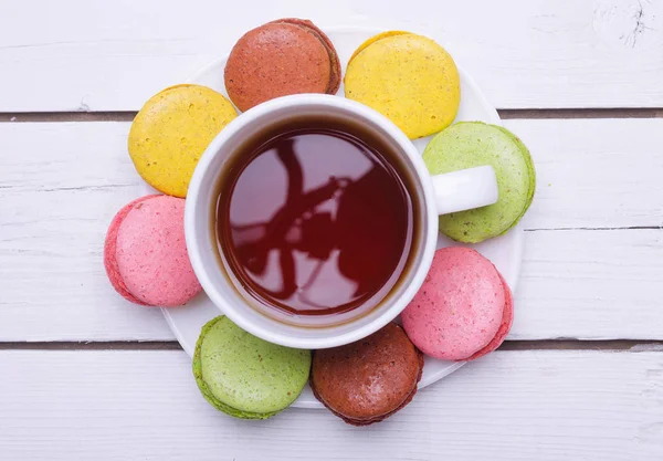 Чашка горячего чая и красочное печенье на деревянном столе . — стоковое фото