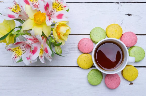 Macarrones multicolores, flores y taza de té caliente en una t de madera — Foto de Stock