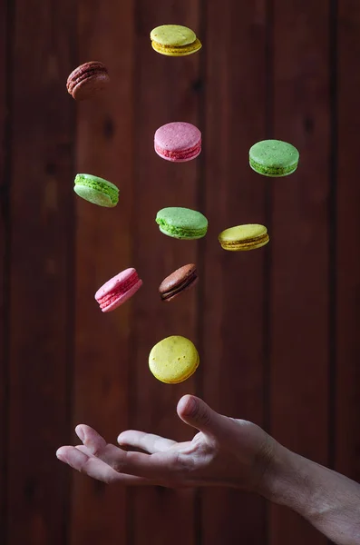 Macarrones moscas multicolores sobre las manos en una mesa de madera, enfoque — Foto de Stock