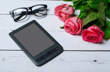 Pembe güller ve ahşap beyaz zemin üzerine tablet.