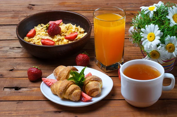 Healthy breakfast: corn flakes, strawberries, tea and croissant.