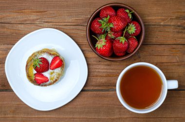 Bir fincan sıcak çay ve bir tatlı çilek ahşap bir sekmesinde