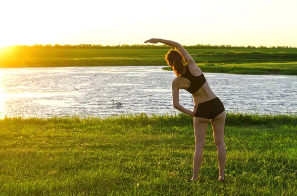 Jovem praticando ioga no lago, amanhecer. Uma vida saudável — Fotografia de Stock