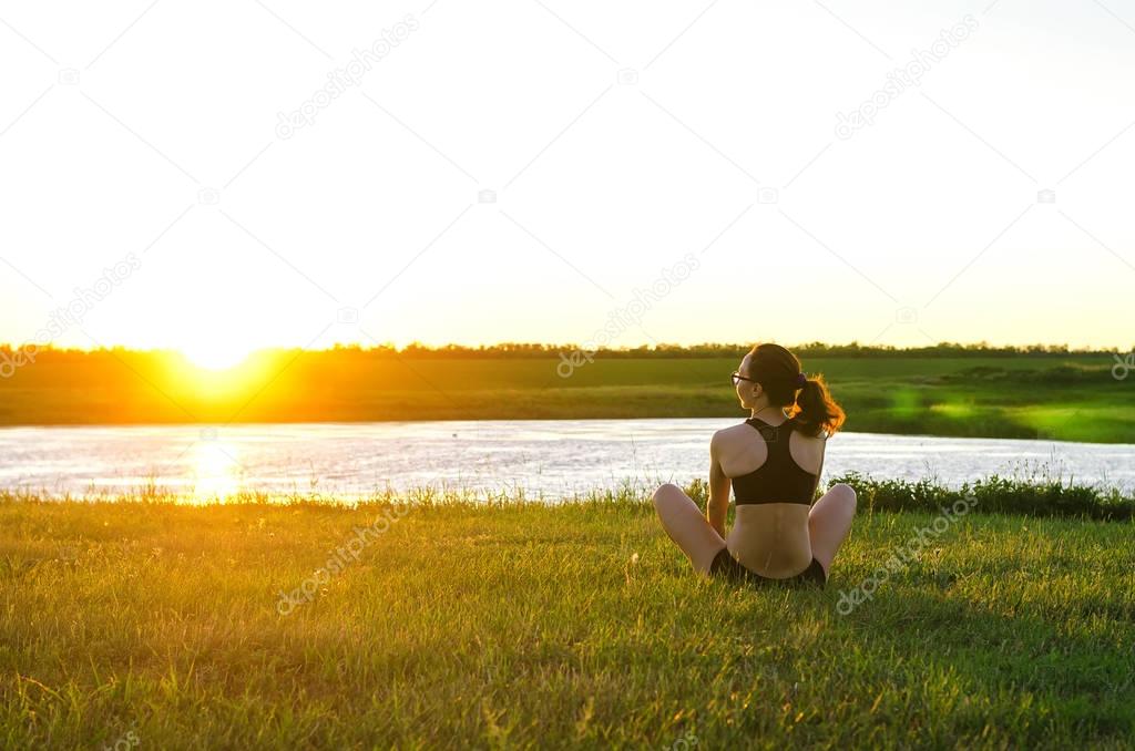 Young woman meditating in lotus position on the river bank, suns