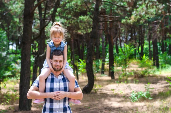 Genç bir baba bir kızı onun omuzlarında, mutlu bir aile tutar.