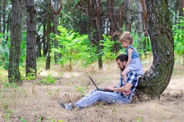 Père et fille sont assis dans les bois avec un ordinateur portable, un frère — Photo