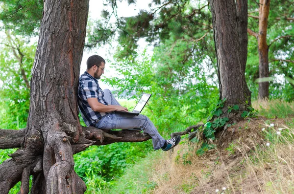 Young man relaxes with laptop sitting in the park, working and r