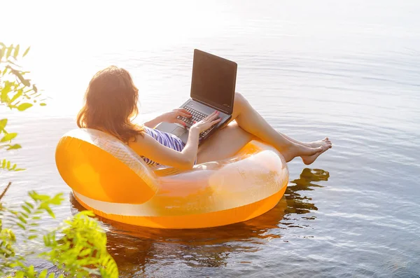 Young woman working on a laptop in the water on an inflatable ri — Stock Photo, Image