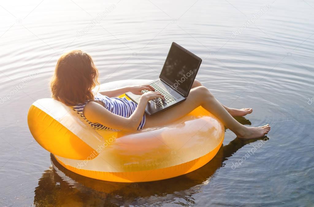 Freelancer works on a laptop sitting in an inflatable ring in th