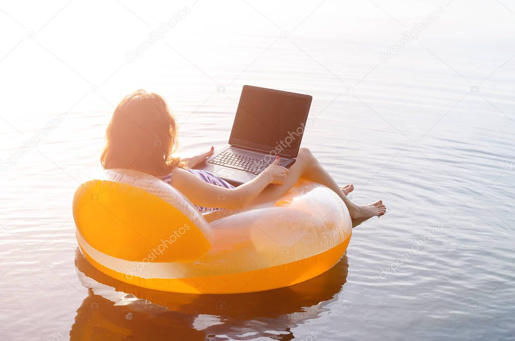 Freelancer works on a laptop sitting in an inflatable ring in th