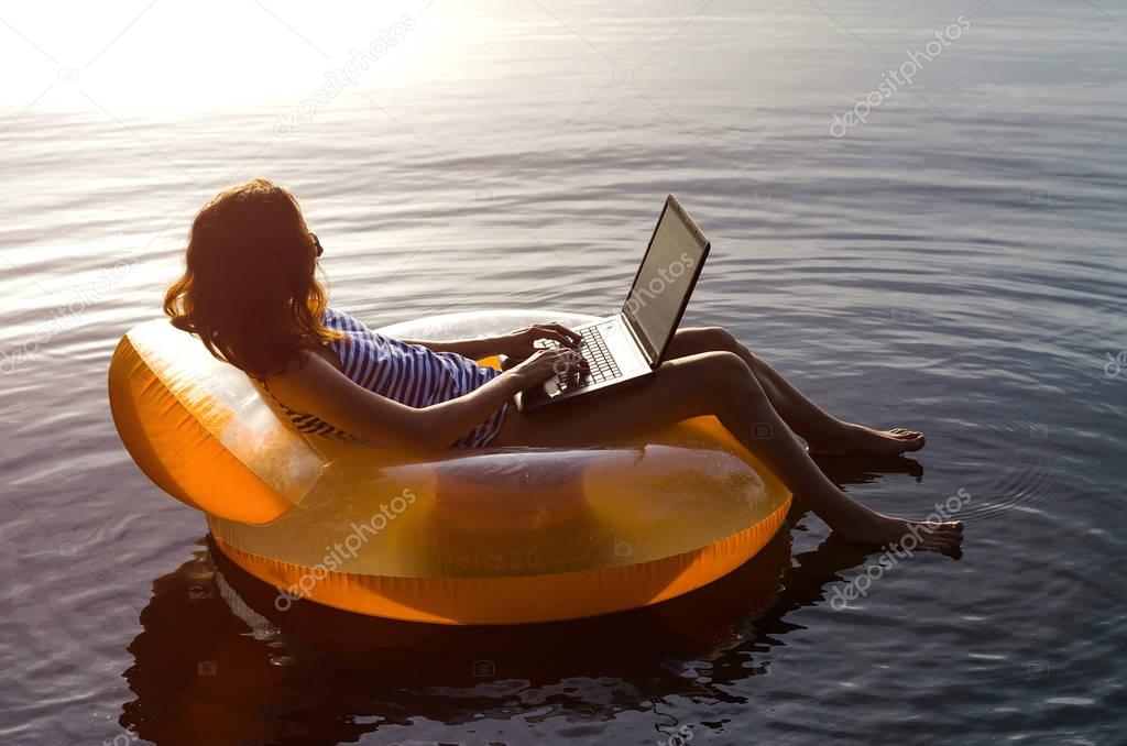 Young woman working on a laptop in the water on an inflatable ri