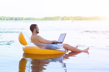 Bir adam bir şişme halka, geri kalan oturan bir dizüstü bilgisayar üzerinde çalışıyor